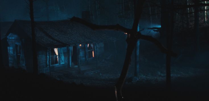 An screenshot of the movie Evil Dead, with an old cabin being in a dark blue forest